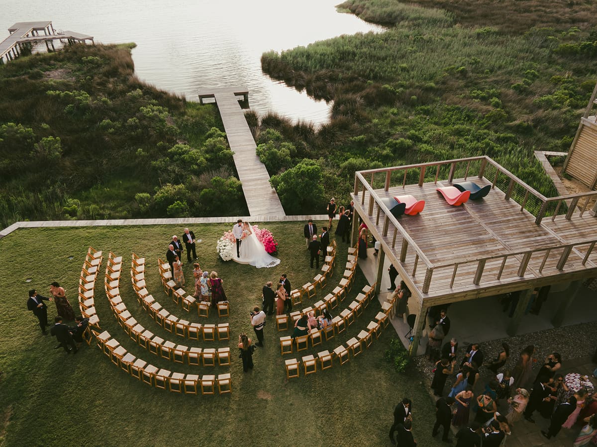 Aerial view of curved rows of chairs on a lawn by the marsh, with a dock leading to the water