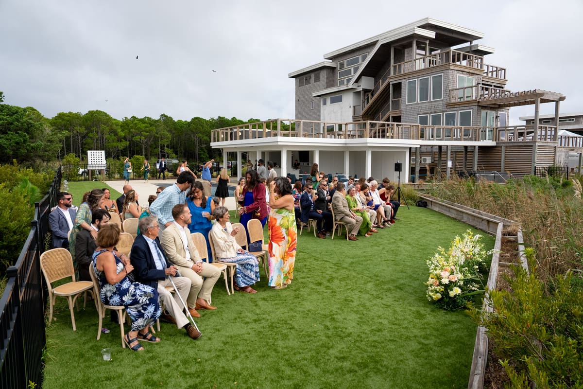 Guests seated on a lawn for a ceremony in front of a large waterfront home