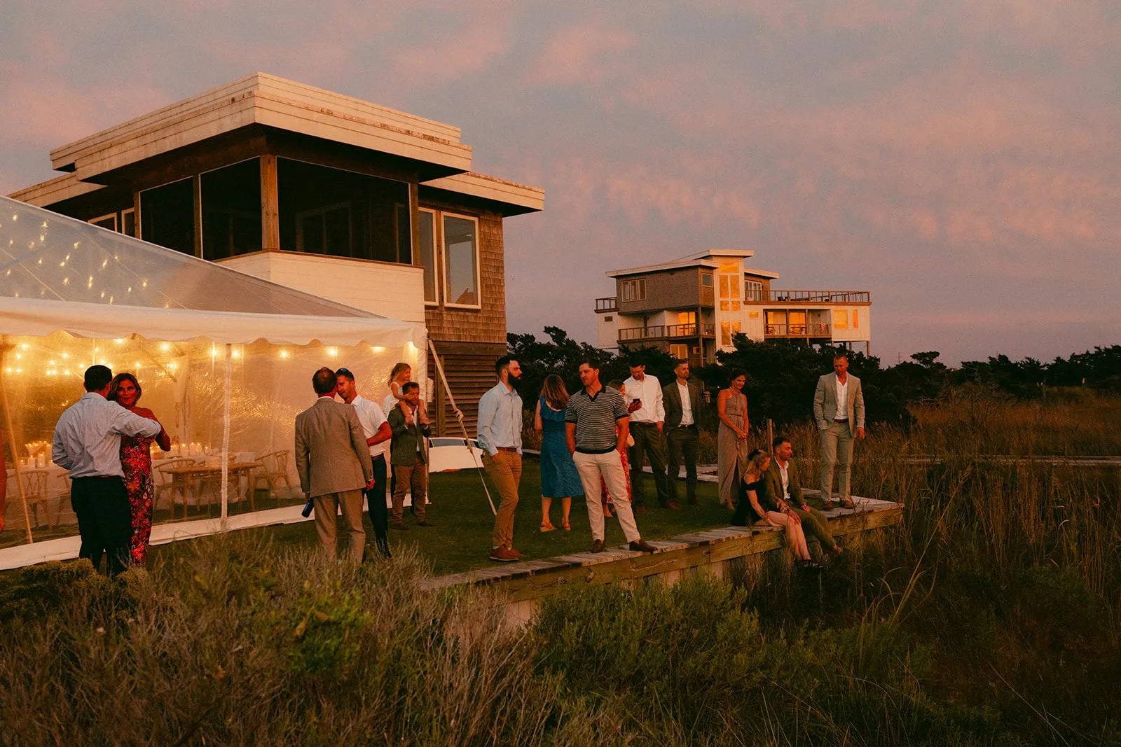 Guests on the boardwalk at golden hour beside the lit tent
